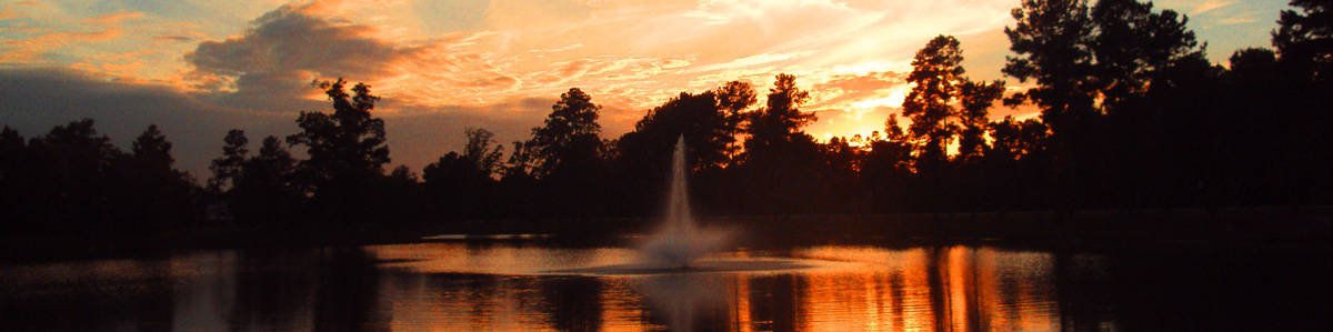 A fountain in the middle of a lake at sunset.
